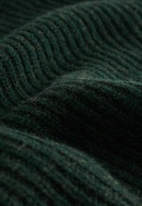 Dunkelgrüner, texturierter Stoff mit dicken Rillenmustern, der eine weiche, flauschige Oberfläche mit subtilen Farbvariationen zeigt.