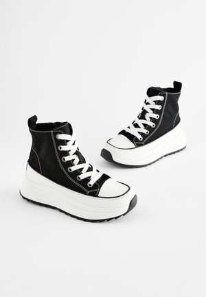 Schwarze High-Top-Sneaker aus Canvas mit weißen Gummisohlen und Zehenkappen, ausgestattet mit weißen Schnürsenkeln und kontrastierenden Nahtdetails.