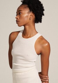 Ribbet, ærmeløs tanktop i cremefarve med en rund halsudskæring og tætsiddende pasform, lavet af blødt, tekstureret stof.