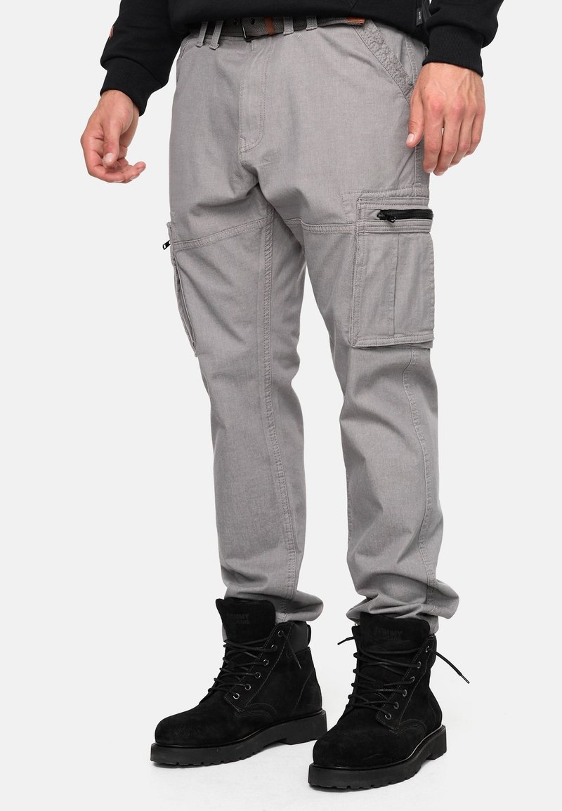Pantalon cargo gris avec poches latérales, fabriqué en matériau léger. Porté avec des bottes noires à lacets, dotées d'une semelle robuste et d'un col rembourré.