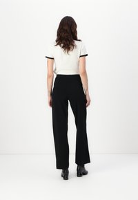 Hvit polo med svart kant, kombinert med løse svarte bukser. Modellen har på seg svarte høye støvler. Minimalistisk design og glatte teksturer.