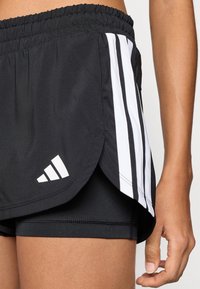 Čierne športové šortky s bielymi pruhmi na bokoch, vyrobené z ľahkého materiálu. Majú elastický pás a viacvrstvový dizajn.