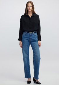 Schwarz langärmliges Shirt, blaue gerade Jeans, schwarzer Gürtel mit dekorativen Beschlägen, schwarze Absatz-Mules, glatte Stoffe, minimalistisches Design.