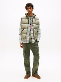Grön pufferväst över en rutmönstrad skjorta, parat med cargobyxor. Bruna skor fulländar outfiten. Texturerade material och flera synliga fickor.
