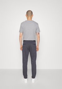 Šedé tričko s krátkým rukávem v kombinaci s námořnickými tepláky. Tepláky mají strukturovanou látku a elastický pas. Bílí tenisky dotvářejí celkový vzhled.