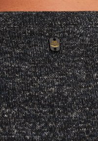 Dunkel gestrickter Pullover mit einem strukturierten Muster, ausgestattet mit einem kleinen schwarz-goldenen Etikett mit der Aufschrift "PME Legend" in der Nähe des Kragens.