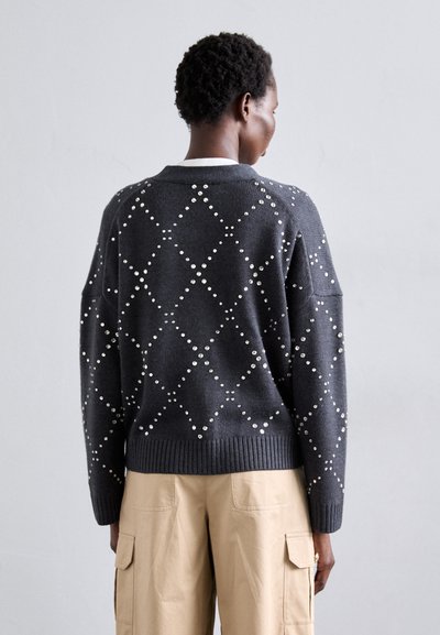 Tumši pelēks adīts džemperis ar dimanta rakstiem, kas izrotāts ar maziem, apaļiem apdariem. Iekļautas kritušās plecu daļas un ribota apakšmala un piedurknes.