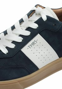 Sneaker navy e bianco realizzato in pelle testurizzata con lacci bianchi, un lato perforato e una suola in gomma beige. Presenta il logo "TMRS".