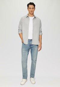 Camicetta a righe grigia con bottoni sopra una maglietta bianca, abbinata a jeans azzurri chiari e sneakers bianche. Design semplice, vestibilità casual.