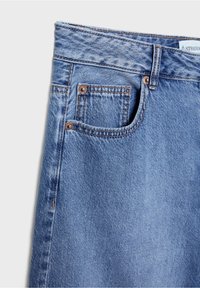 Jeans de denim azul claro con un diseño tradicional de cinco bolsillos, detalles de costura, remaches de tono cobre y una textura ligeramente desvaída.