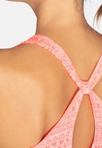 Top deportivo coral con textura estampada, que presenta un diseño de espalda entrecruzada. La tela suave y las tiras delgadas resaltan un ajuste cómodo.