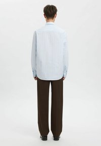 Šviesiai mėlyna dryžuota marškiniai su ilgomis rankovėmis, apvaliu apačiu ir saginėtomis rankogaliais, derinami su rudais plačiomis kojomis kelnėmis. Tekstūruota medžiaga, laisvalaikio dizainas.