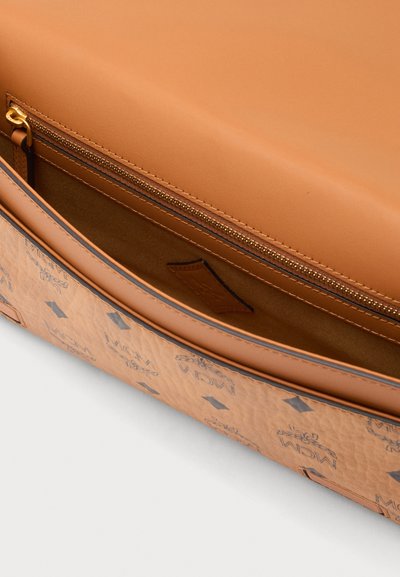 Sac de designer en cuir marron ouvert pour montrer le compartiment intérieur zippé et la surface extérieure imprimée avec le motif du logo MCM.