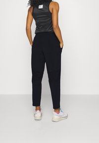 Sorte joggers med en afslappet pasform, elastisk talje og sidelommer, parret med en ærmeløs sort top og lysfarvede sneakers.