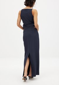 Navy-blaues ärmelloses Top kombiniert mit einem passenden High-Waist-Rock, der über einen seitlichen Schlitz und ein elegantes Design verfügt; das Model trägt schwarze Absatzschuhe.