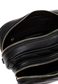 Borsa in pelle nera con texture acolciata, dotata di diverse tasche con zip e dettagli in hardware dorato. L'interno è foderato in tessuto nero.