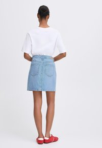 Light blue denim skirt with five pockets and a mid-length design, paired with a plain white T-shirt and red slip-on shoes.