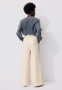 Haut gris à manches longues avec une coupe décontractée, associé à un pantalon large beige clair. Texture douce et design minimaliste.
