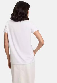 Biała koszulka z okrągłym dekoltem i krótkimi rękawami, wykonana z miękkiego materiału. Tył ma gładki, prosty wzór bez ozdób.