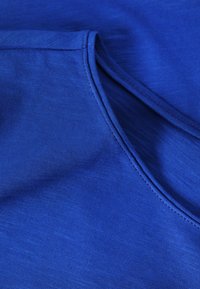 Gros plan sur un tissu bleu à col en V montrant une couture fine et une texture douce en coton.
