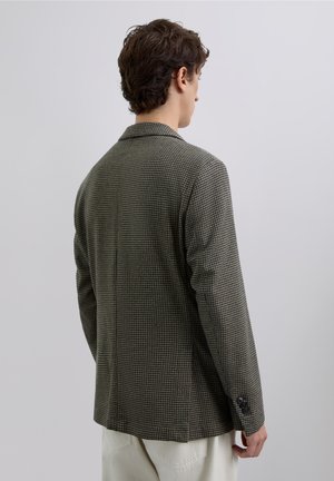 Blazer de cuadros tipo houndstooth en verde oscuro y beige, con corte entallado y solapas de pico; cuenta con puños de dos botones y una abertura sencilla en la parte posterior.