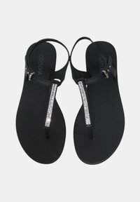 Sandali piatti neri con design a infradito, caratterizzati da una cinghia verticale decorata con strass e suola in gomma liscia. Cinghie regolabili alla caviglia.