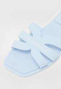 Ljusblå sandal i mjukt material med lager av tvärgående remmar och platt sula. Har Karl Lagerfeld-logotyp i vitt.