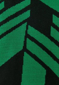 Tissu de pull tricoté vert et noir présentant des motifs géométriques en zigzag audacieux. La texture est lisse, avec une apparence serrée.