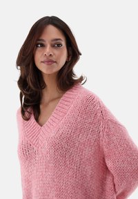 Rosa gestrickter Pullover mit tiefem V-Ausschnitt und lockerer Passform. Verfügt über ein strukturiertes Muster und weine Wolle für ein gemütliches Aussehen.