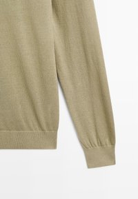 Beige långärmad stickad tröja med ribbade manschetter och midja på en vit bakgrund.