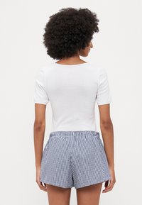 Witte top met korte mouwen gecombineerd met blauwe en witte gingham-check shorts. De stof lijkt licht en ademend, met een elastische tailleband.