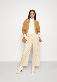 Beige wide-leg trousers, white fitted turtleneck, and a camel blazer. Beige ankle boots with block heels. Smooth fabric, tailored design.