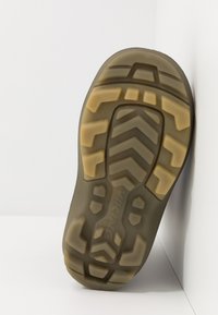 Suela de zapato de goma con un patrón de banda de rodadura en zigzag. Base de color gris oscuro y acentos de goma marrón claro. Texturizada para proporcionar agarre y tracción.