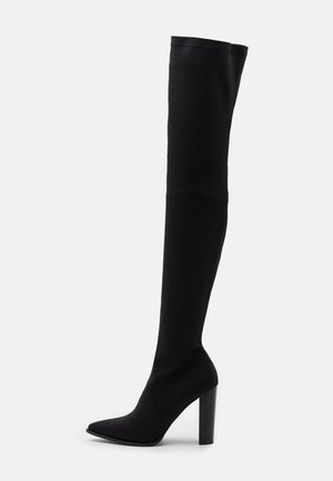 Bottes noires cuissardes en tissu extensible avec bout pointu, talon carré haut et design sans coutures. Texture lisse sans embellissements.
