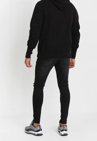 Felpa nera con tasca a canguro, abbinata a jeans neri aderenti con dettagli strappati. Calzature: sneakers sportive grigie.