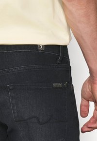 Tumma siniset farkut, joissa on klassinen malli viidellä taskulla, hienovaraisilla saumoilla ja merkkilappu takataskussa.