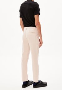 Světle růžové kalhoty s úzkým střihem, rovnými nohavicemi a detailem zadních kapes. Nošené s černým tričkem a černými dřeváky.