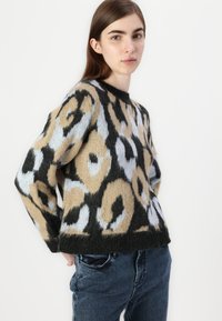Knit sweater featuring an abstract animal print in beige, black, and light blue. Boxy shape with a rounded neckline and long sleeves.