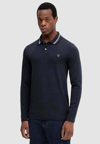 Granatowa koszulka polo z długim rękawem, białym kołnierzem w paski, plisą na trzy guziki oraz małym trójkątnym logo na lewej piersi. Miękka tkanina.