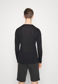 Black long-sleeve shirt with a slight sheen, soft texture, and rounded neckline, worn with dark shorts, viewed from the back against a white background.