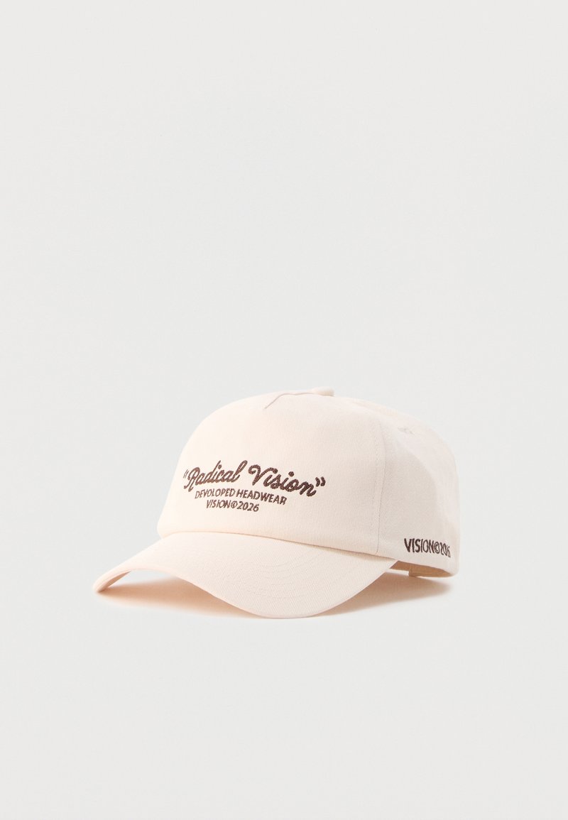 Casquette de baseball crème avec texte marron indiquant "Radical Vision" et "Developed Headwear Vision© 2026" à l'avant et sur le côté.
