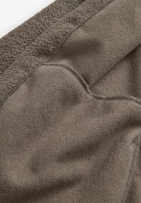 Țesătură din fleece într-o nuanță gri-maro estompată, cu o textură netedă; prezintă o margine pliată și detalii de cusătură subtile.