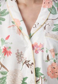 Floral pajama top in lightweight fabric. Features pink, green, and brown floral patterns. Includes a chest pocket and yellow piping on the collar.