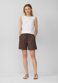 Top sin mangas blanco con escote barco, combinado con pantalones cortos marrones a la rodilla con cintura elástica y puños doblados.