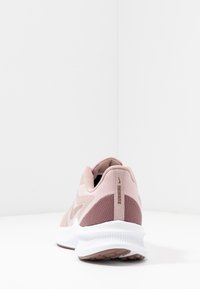 Baskets de course en maille rose clair avec des accents rose foncé, une semelle blanche rembourrée et un panneau arrière texturé portant le mot "RUNNING" en beige.