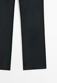 Onderkanten van zwarte recht gesneden broeken plat weergegeven op een witte achtergrond.