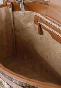 Bežová taška přes rameno uvnitř se hladkým povrchem, obsahující zipovou kapsu a reliéfní vzor loga na podšívce. Hnědé kožené akcenty po celém obvodu.