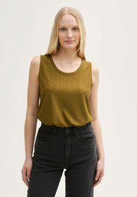Olivgrön ärmlös topp med texturerad mönster, rund halsringning och avslappnad passform. Matchad med högmidjade svarta jeans.