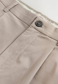 Beige Baumwollhosen mit einer glatten Textur, versehen mit einer Vordertasche, Knopfverschluss und dezenten Ziernähten.