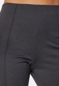 Pantaloni aderenti grigio antracite con una texture liscia, caratterizzati da una vita alta e linee di piega sottili che scorrono lungo i pannelli frontali.